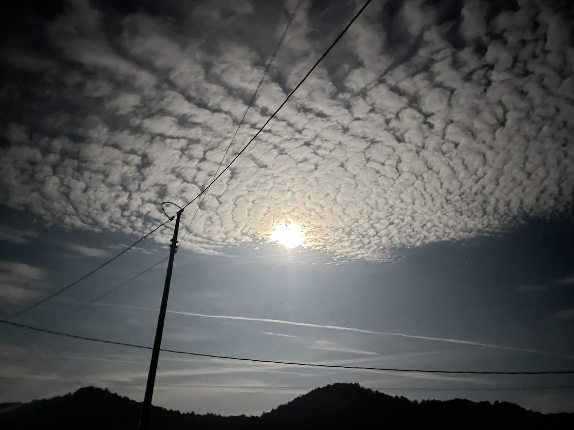 The moon behind a sky of mackerel cloud, above the dark ridge.